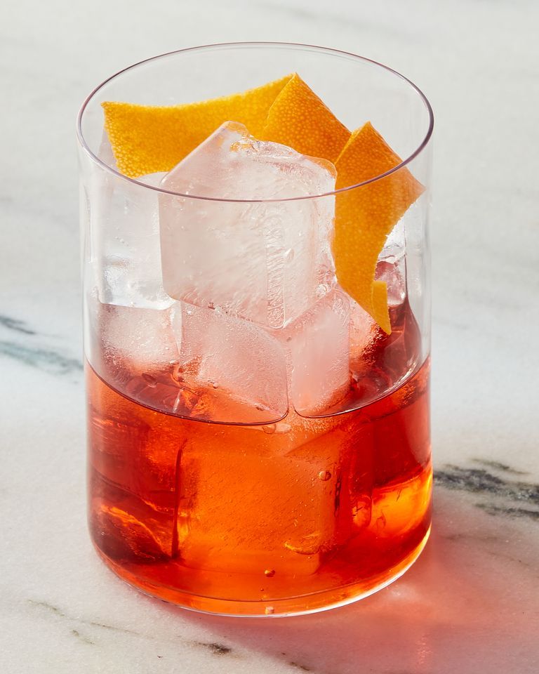 glass of negroni cocktail garnished with an orange peel on a white marble background