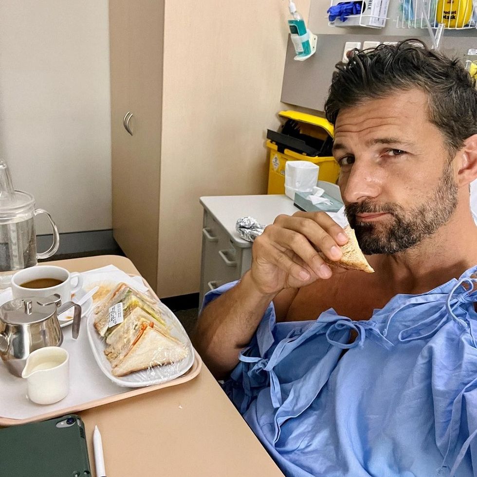 neighbours actor tim robards sits in a hospital bed with a plate of sandwiches after having football accident