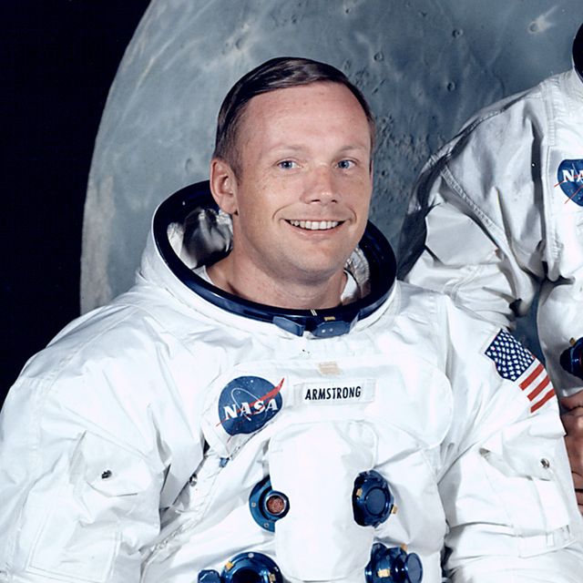 astronauts neil armstrong, michael collins, and buzz aldrin pose for a photo while wearing their white nasa space suits, neil and buzz are sitting on either side of michael who stands in the middle, behind them is a large photo of the moon