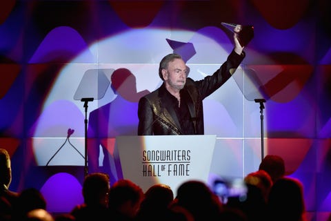 neil diamond holding a trophy and waving to the audience