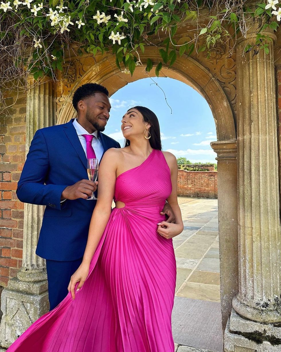 nelly london and her boyfriend b smile at one another at a wedding