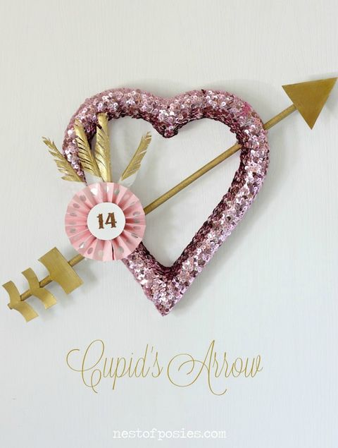 wreath in a heart shape with pink sequins, a gold arrow through it, gold dipped feathers and a round 14 sign