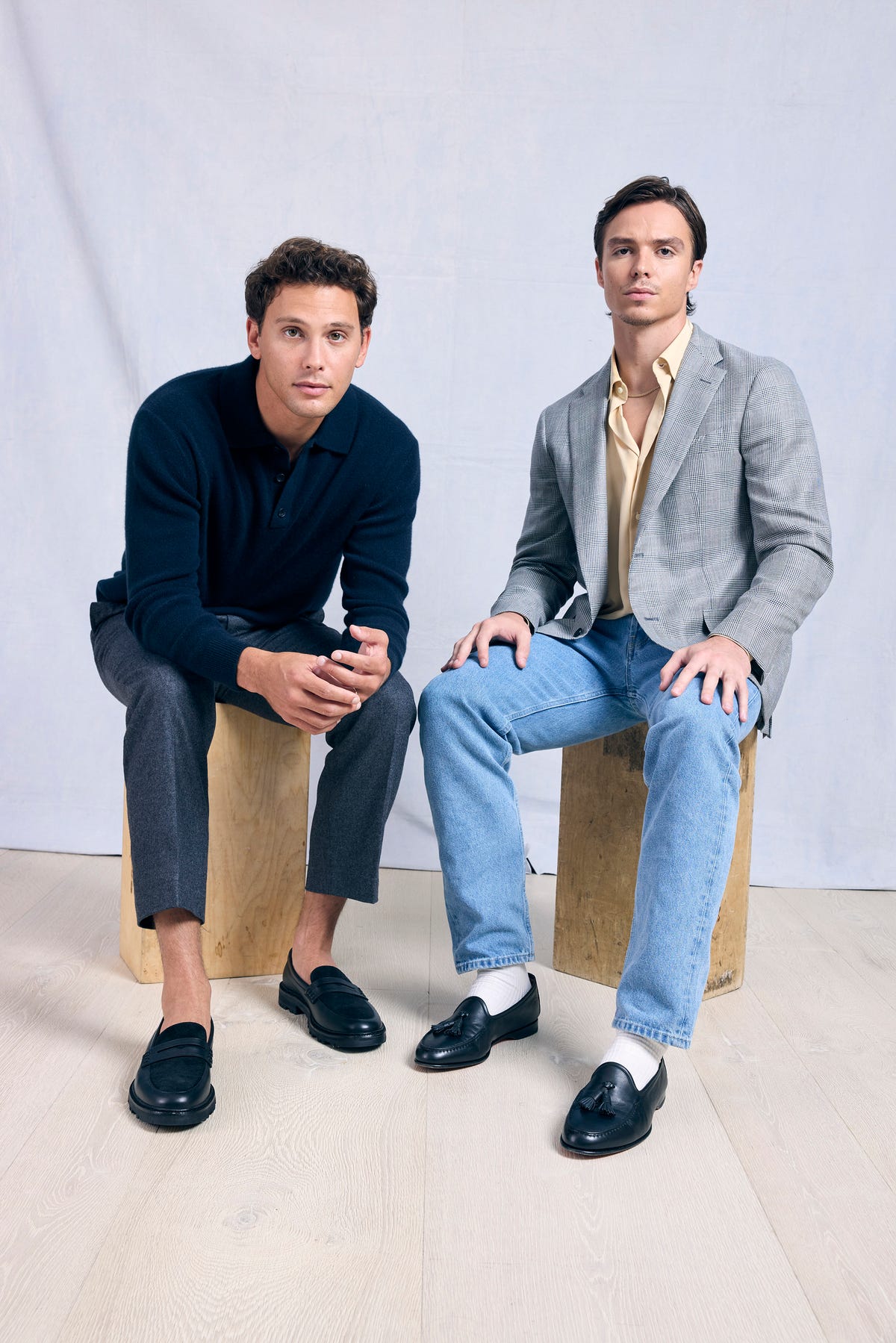 two men sit on wooden blocks and star at the camera