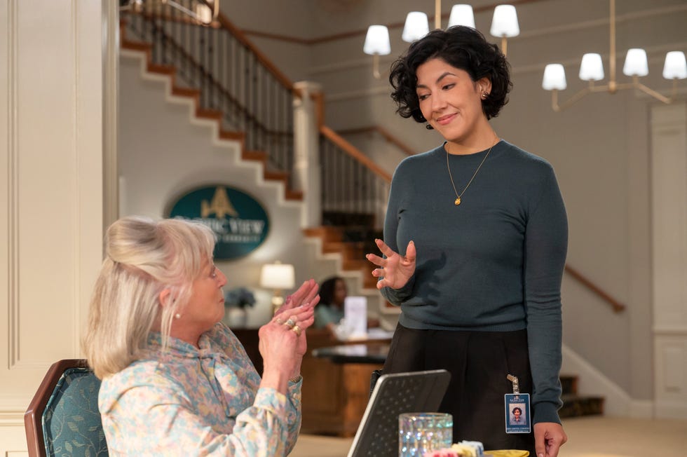 Susan Ruttan as Gladys and Stephanie Beatriz as Didi gesture towards each other at the reception of a retirement home in a scene from “A Man On The Inside” on Netflix.