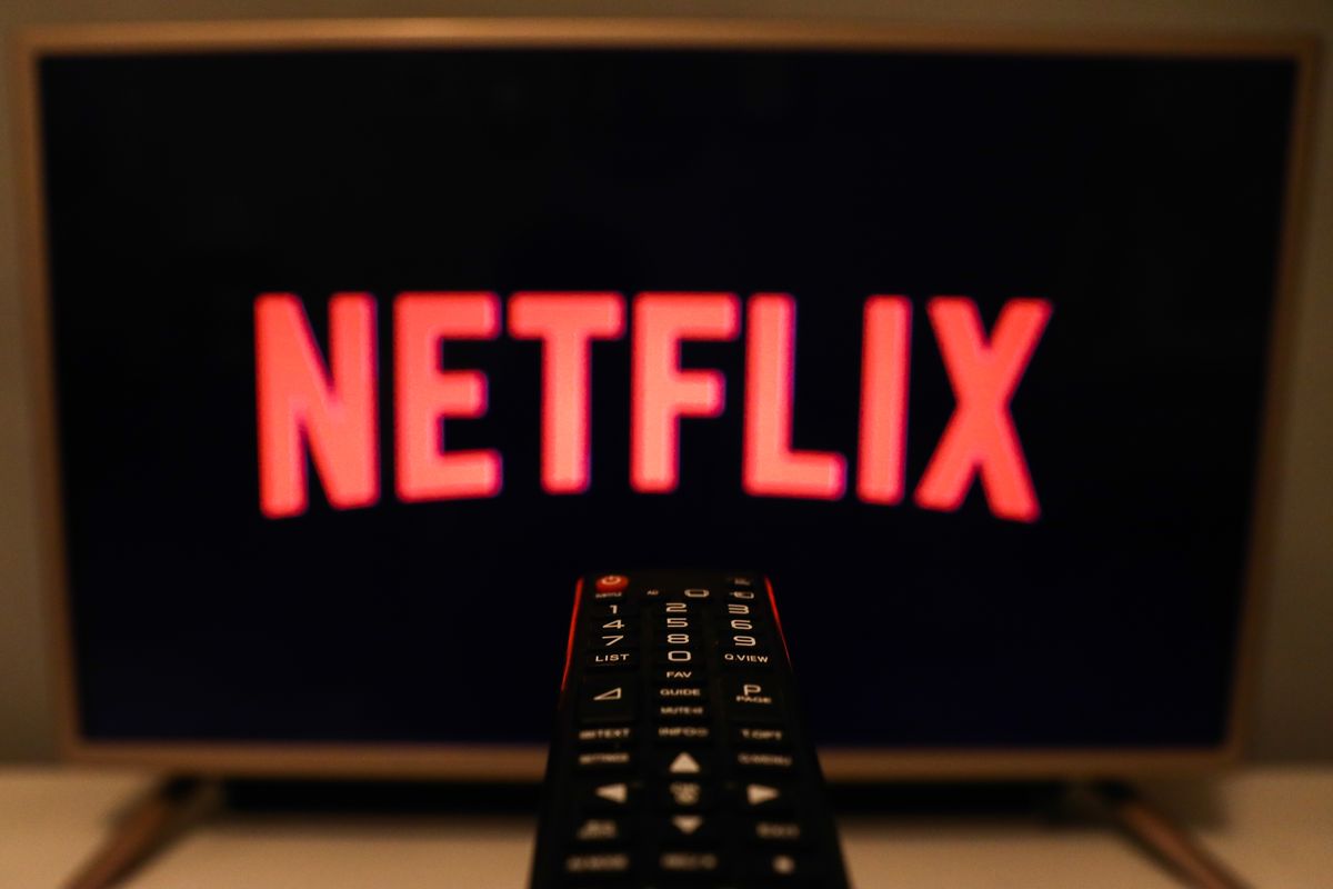 netflix in red against a black background with a remote control in the center of the foreground