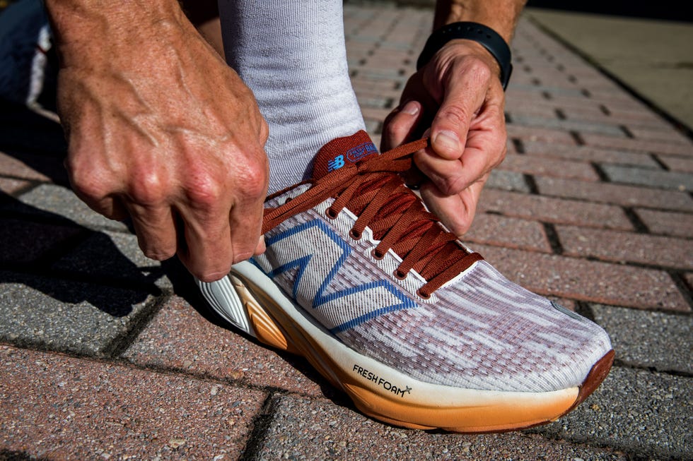 a person tying the laces of a running shoe on a brick surface