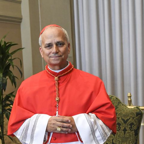 a man in red and white robes smiles with his hands clasped in front of him