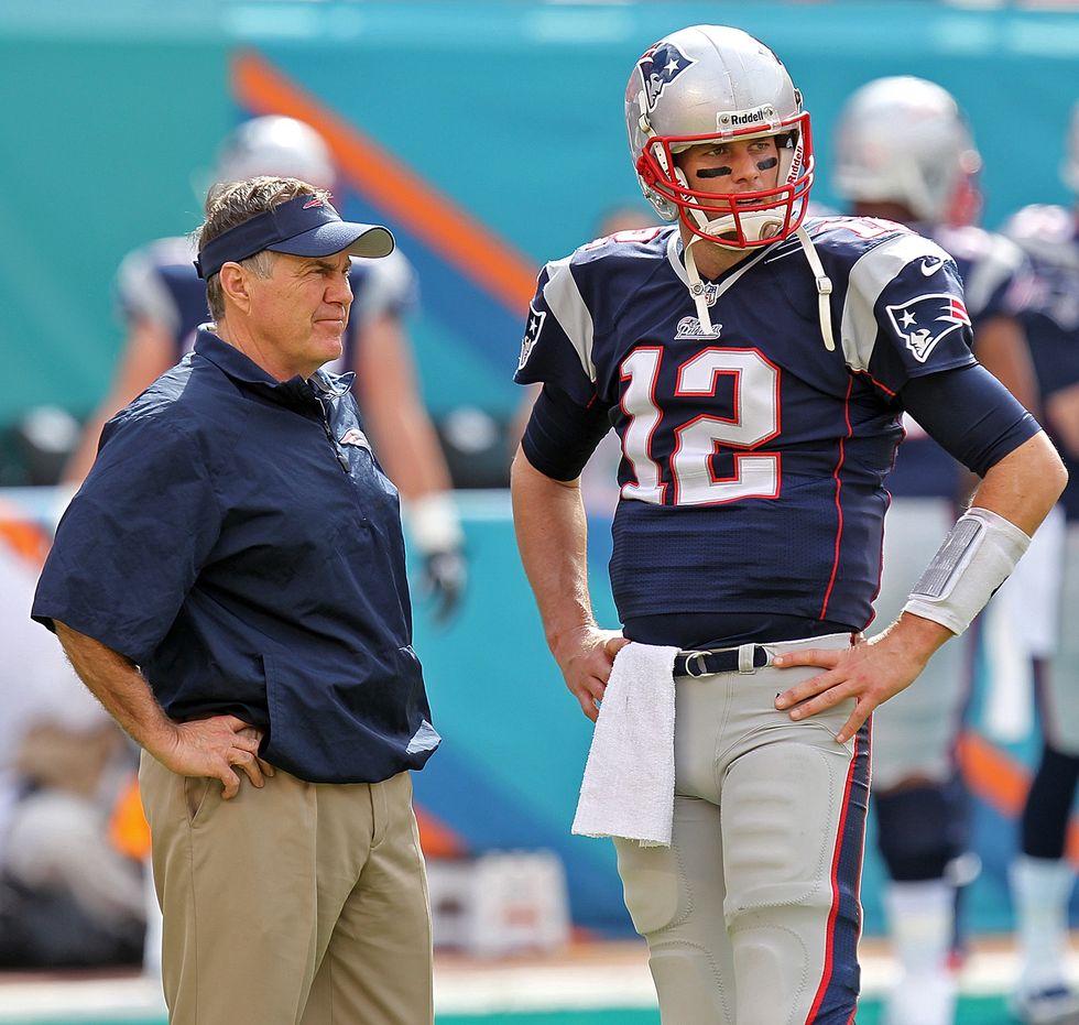 bill belichick and tom brady standing on the sideline during a football game