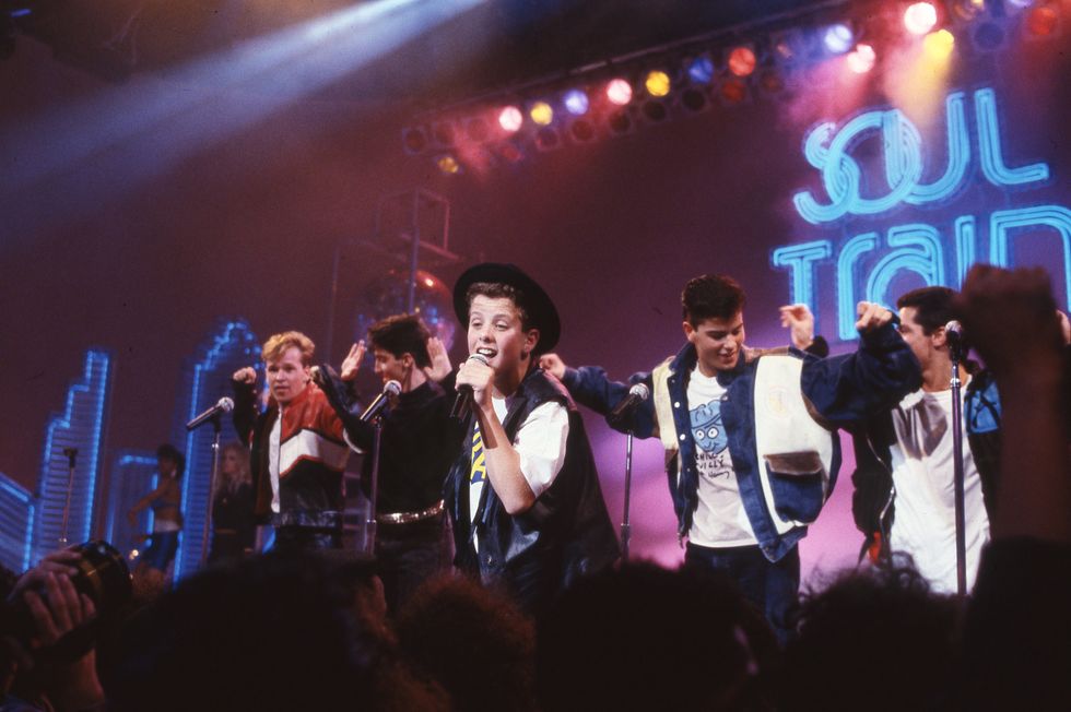 new kids on the block members sing and dance on a stage with a soul train logo in the background and a crowd in front of them