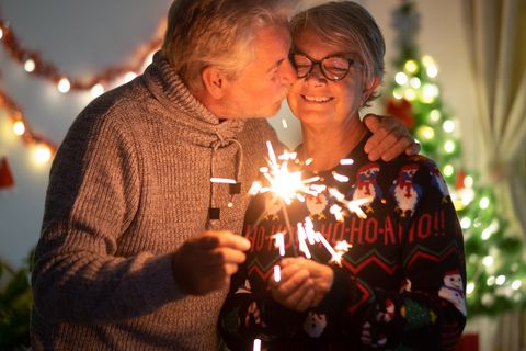 an affectionate kiss between elderly wife and husband who celebrate christmas with sparks lights and christmas tree in the background