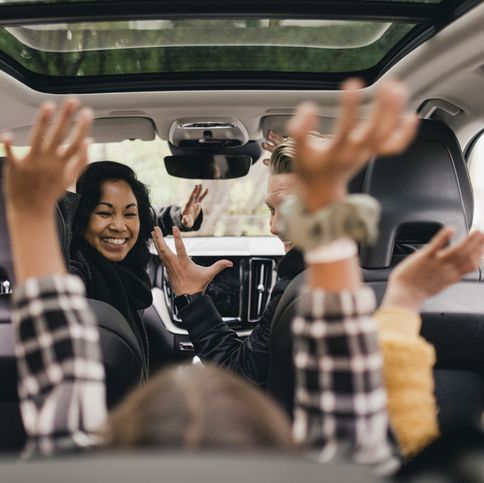 cheerful family raising hands while enjoying road trip in electric car