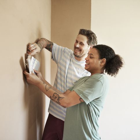 happy multi ethnic couple comparing color swatch with wall