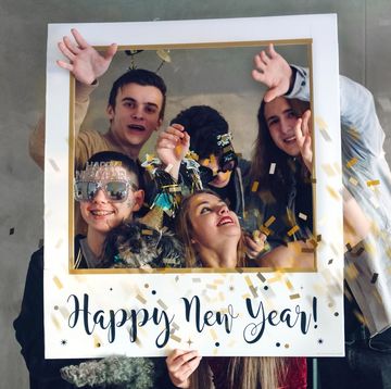 teens in new years party gear posing in a giant polaroid style frame with happy new year wishes written across bottom