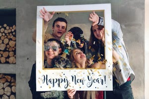 teens in new years party gear posing in a giant polaroid style frame with happy new year wishes written across bottom