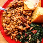 stewed black eyed peas on a red plate, alongside greens and buttered cornbread, all on a wooden surface