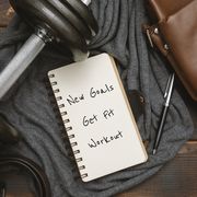 new year's goals and resolution written on notepad, with dumbbell and satchel man's bag on rustic wood