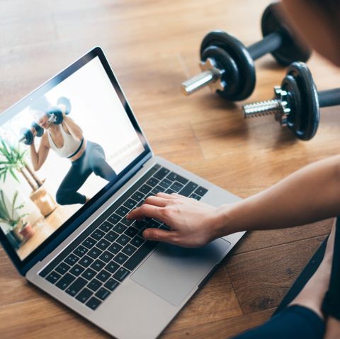 high angle view of young asian woman practising weight training workout at home with a video lesson on laptop during the day