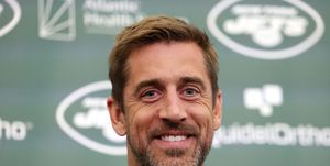 aaron rodgers smiles at the camera, he wears a black polo shirt with a green accent on the collar