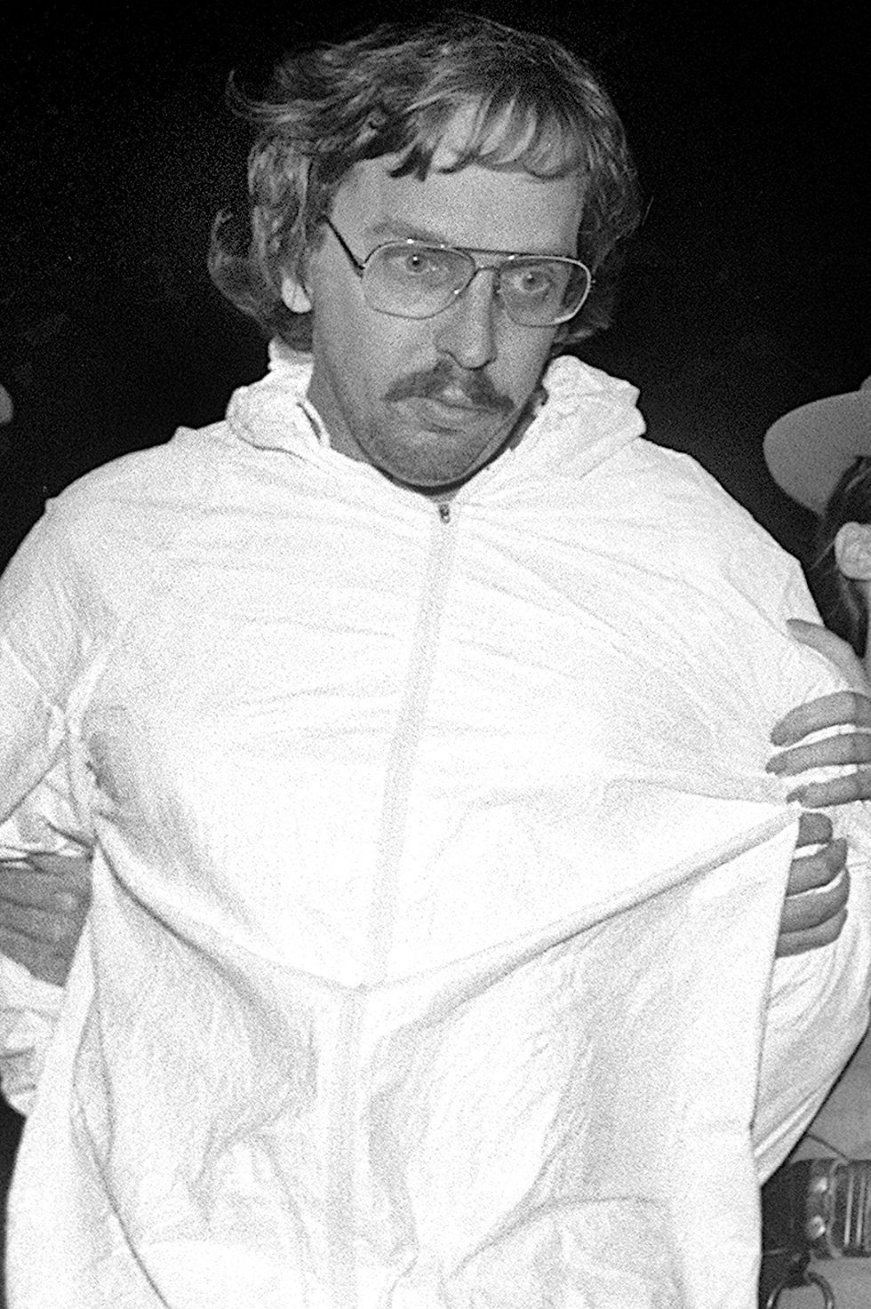 joel rifkin being led by police officers wearing a white jumpsuit