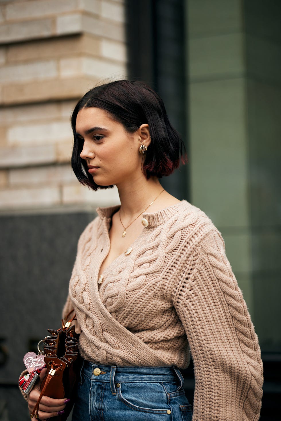 woman wearing a knitted sweater and highwaisted jeans holding a small handbag best brunette bob haircut for summer