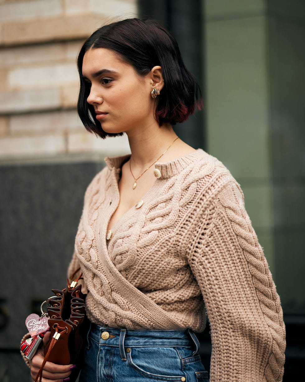 woman wearing a knitted sweater and highwaisted jeans holding a small handbag best brunette bob haircut for summer
