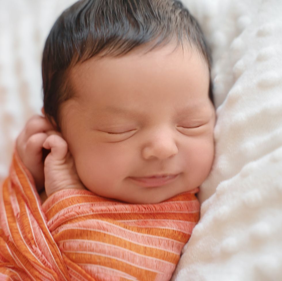 multicultural baby names, newborn baby infant with dark hair smiling lying on side sleeping. cute little middle eastern child on blanket. tranquil scene close up