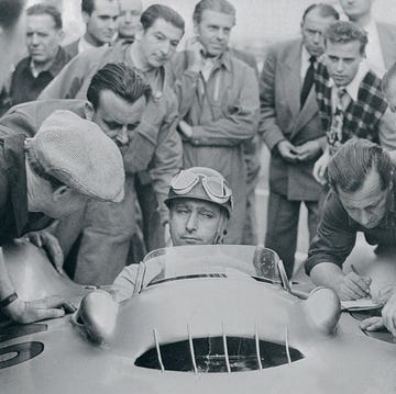 newsmen and mechanics surround driver juan manuel fangio