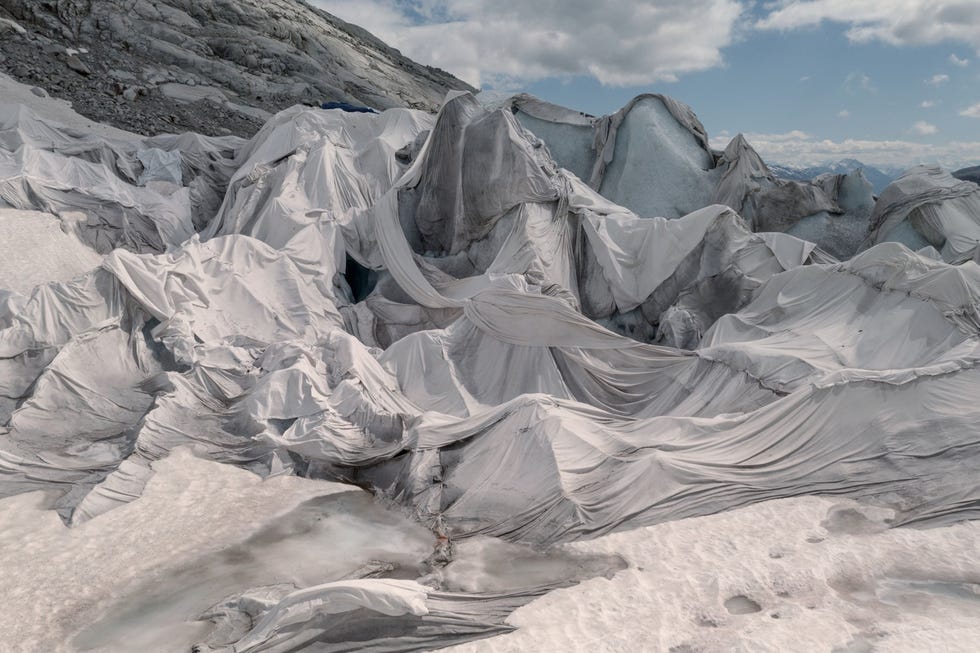 De tong van de Rhnegletscher in Zwitserland is afgedekt met zonwerend plastic Een grot die hier elk jaar in het verschuivende ijs wordt uitgehakt trekt al sinds 1870 toeristen aan Voorlopig blijft er dankzij de afdekking het hele jaar door genoeg ijs bewaard om de grot te handhaven