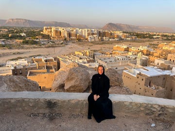 in een zwarte abaya, met op de achtergrond de wereldberoemde, lemen wolkenkrabbers van shibam