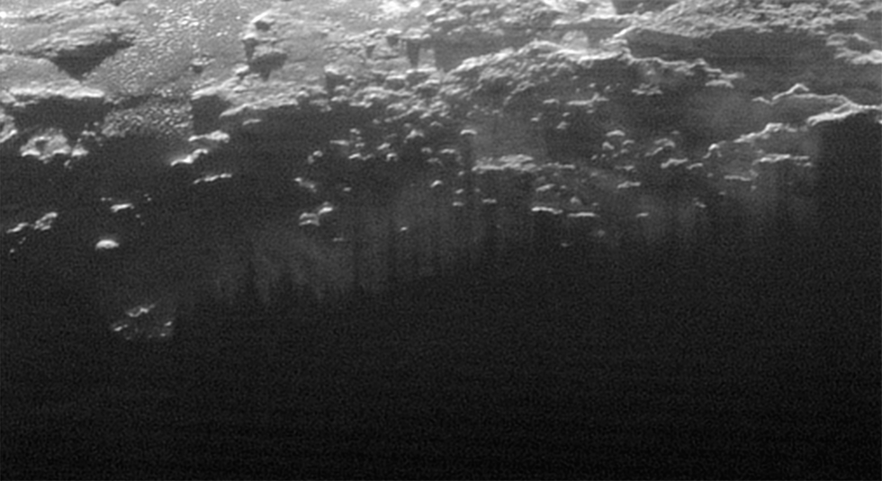 De ondergaande zon verlicht een mistlaag of laaghangende nevel die wordt doorsneden door de parallel lopende schaduwen van de vele heuvels en lage bergen op Pluto  NASAJHUSwRI
