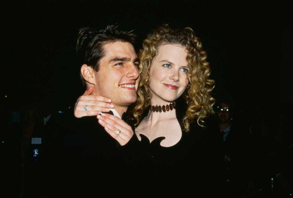 tom cruise and nicole kidman smile as they look to the right, kidman has her hands wrapped around cruises neck, they both were black formal attire