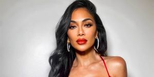 nicole scherzinger in front of a white backdrop wearing a red top and skirt and lipstick with long dark hair and hoop earrings