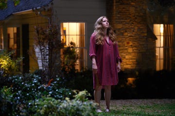 amy adams in nightbitch, a woman stands in a nightdress outside a house at night and looks up to the sky