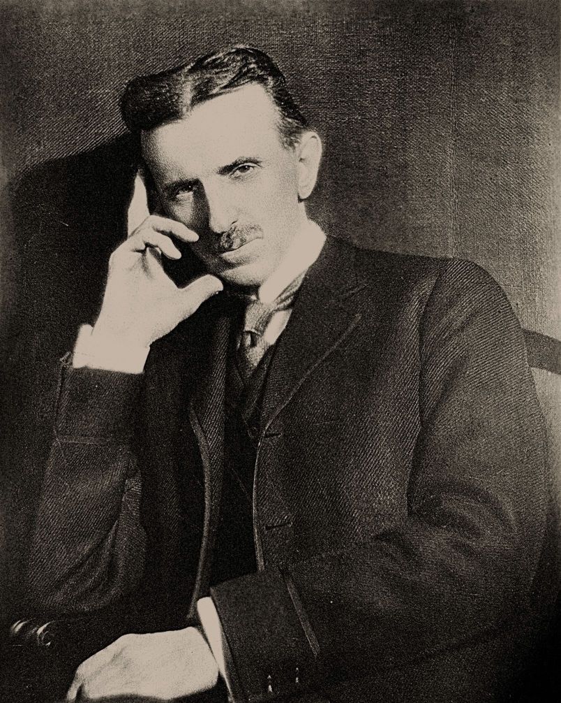 nikola tesla sitting down in a photograph and holding his head with his right hand in a thinking posture