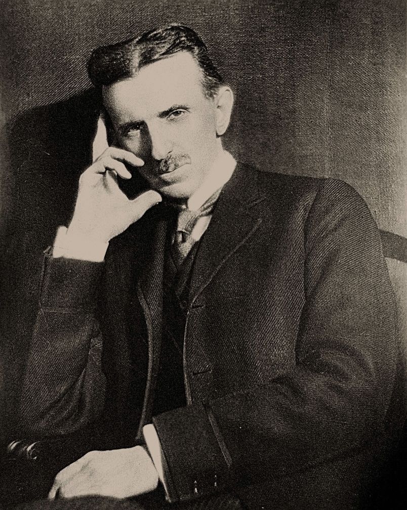Nikola Tesla sentado en una fotografía y sosteniendo su cabeza con su mano derecha en una postura de pensamiento.