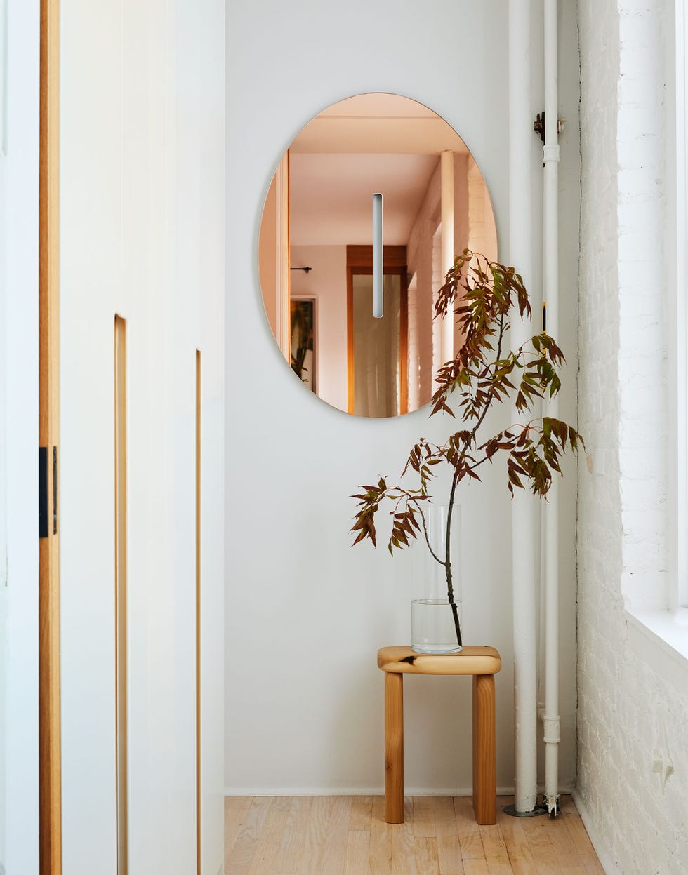 a modern entryway with a round mirror a wooden stool and a vase with a plant