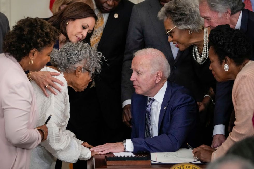 opal lee, wearing a white outfit, talks to a seated joe biden, who places his hands on hers, among a crowd of listening people, including kamala harris