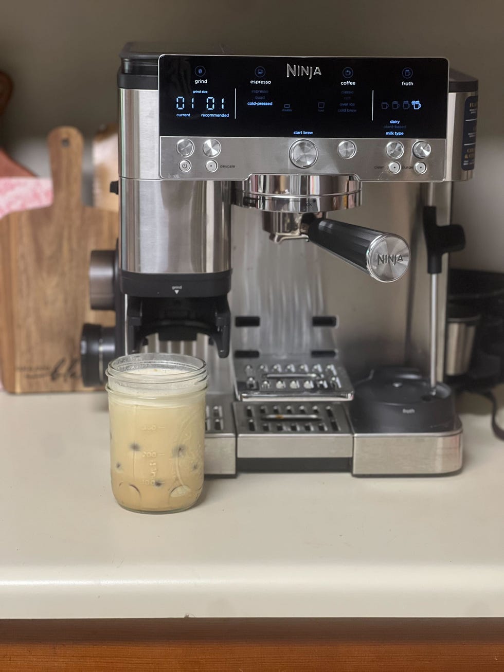 a black and silver espresso machine on a kitchen counter with an iced coffee sitting next to it