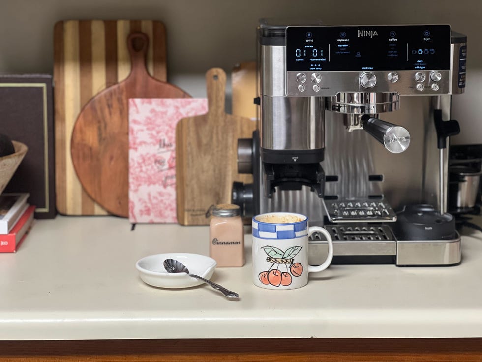 a silver and black espresso machine sitting on a kitchen counter next to a mug of coffee