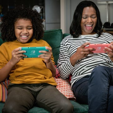 two individuals sitting on a couch playing handheld video games