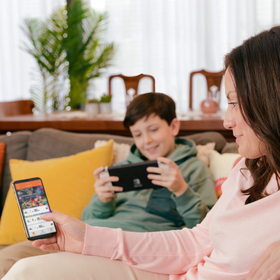 a person using a smartphone while another individual plays a handheld device on a couch