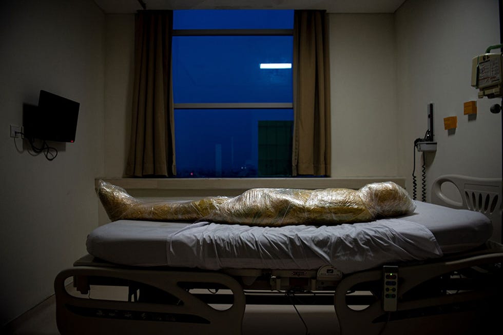 Jakarta, Indonesia JAKARTA INDONESIIn Jakarta Indonesi ligt het gebalsemde lichaam van een COVID19slachtoffer nog op een ziekenhuisbed in afwachting van een lijkenzak Twee verpleegsters hadden circa een uur nodig om de dode in plastic zeil te wikkelen een maatregel die is bedoeld om de verspreiding van het coronavirus tegen te gaan Indonesirs waren geschokt toen ze de foto zagen want hij toont het menselijke aspect van de verschrikkingen die de pandemie met zich meebrengtDuidelijk is dat de kracht van dit beeld de discussie over het coronavirus heeft aangezwengeld zei fotograaf Joshua Irwandiin juli 2020 tegen National Geographic We moeten de opofferingen en de risicos voor artsen en verplegers opnieuw afwegen