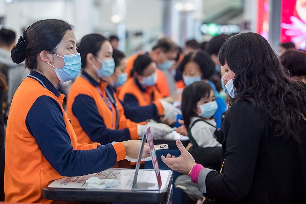 Medewerkers van de spoorwegen in Hongkong in oranje hesjes en met mondkapjes controleren de identiteitsbewijzen van reizigers op het station van Kowloon Hongkong is een van de plekken waar met het coronavirus besmette patinten zijn opgedoken sinds de griepachtige ziekte uitbrak in centraal China