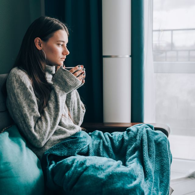 no central heating, cold apartment young brunette woman drink hot tea, look out the window, wrapped in a blanket in cold apartment