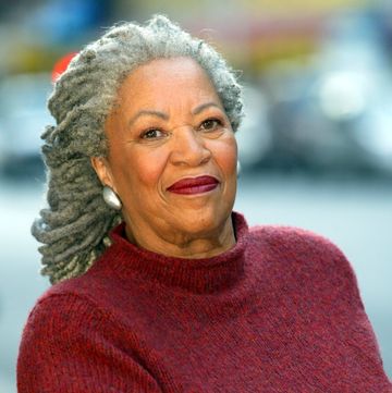 a woman with gray dreadlocks smiles at the camera, she wears a red knit sweater and silver earrings