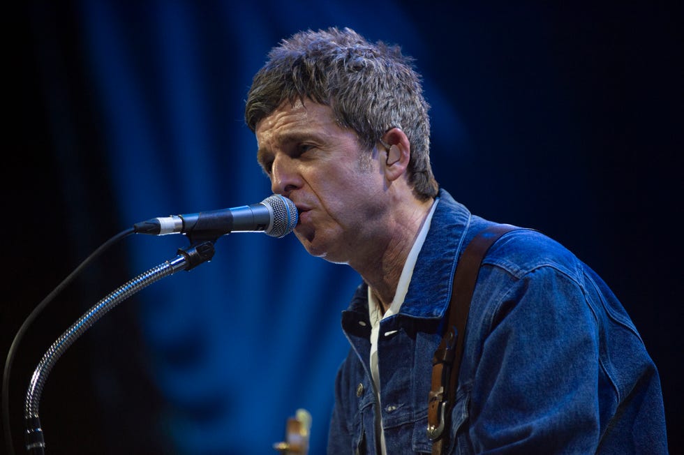 noel gallagher signing as he leans in close toward a microphone