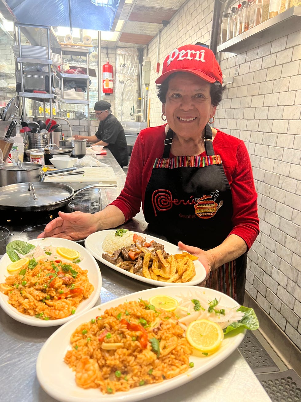 a woman serves three plates of seafood rice and grilled meat dishes in a restaurant kitchen