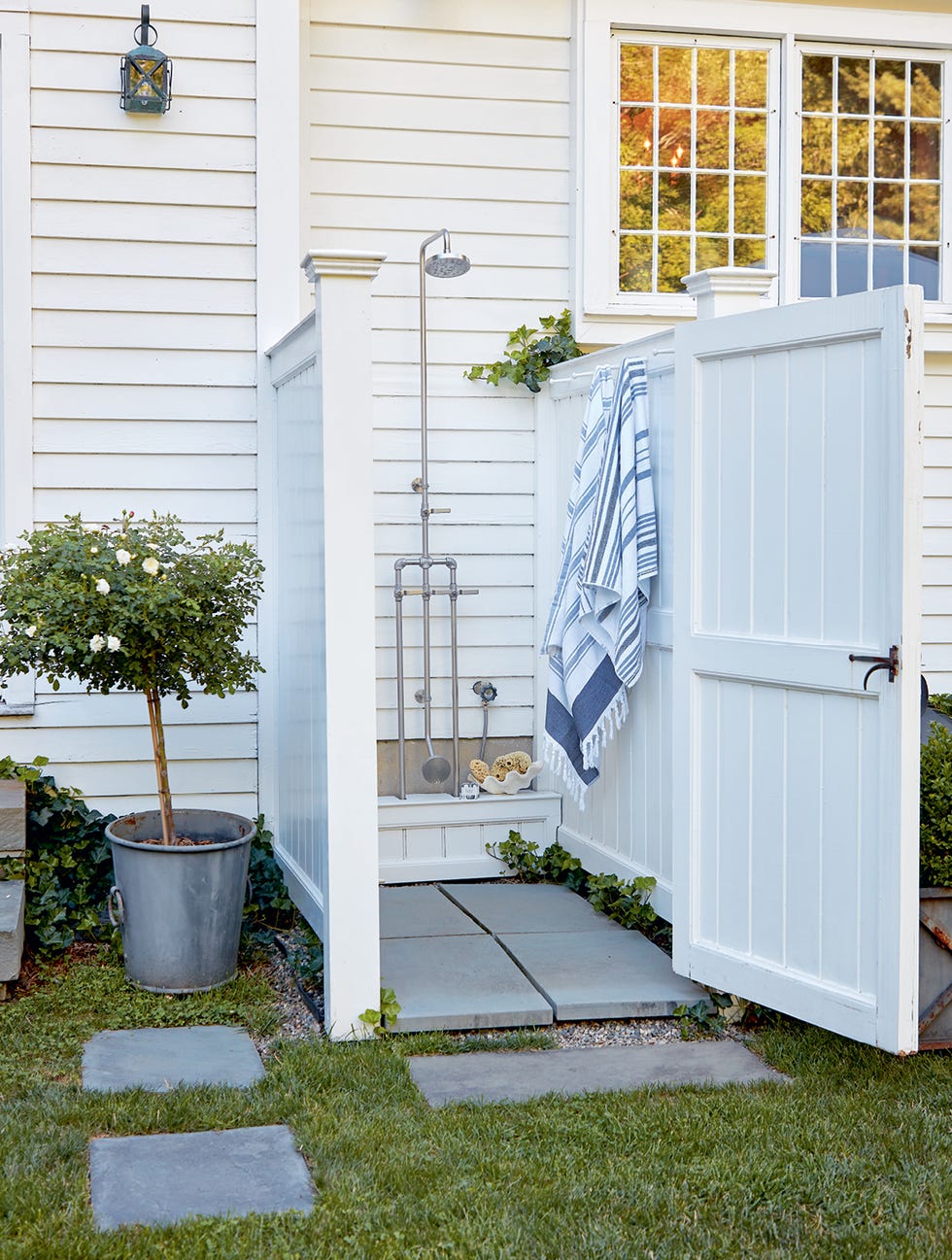 a white outdoor shower enclosure with stone pavers