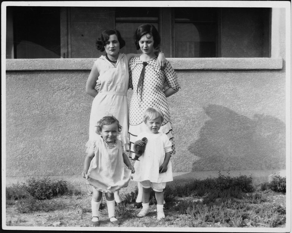 marilyn monroe as a toddler stands in front of her mother gladys baker in front of a house, they are joined by another toddler on the left of marilyn and another woman, who gladys wrapped her right arm around