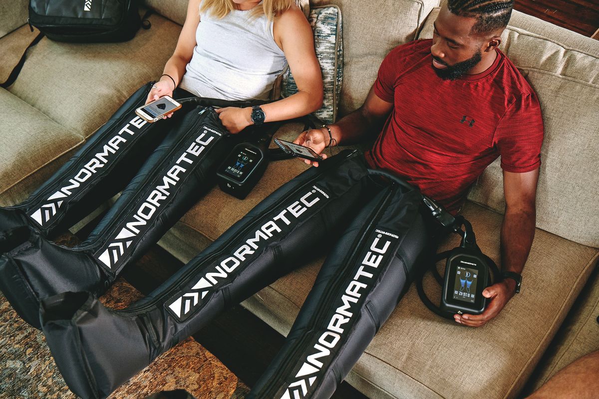 two people sit on couch in normatec boots